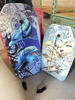 Two boogie boards standing upright, dolphin and shark graphics visible, leashes attached