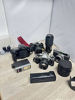 Group shot of four cameras, telephoto lens, flash, cases, film canisters.
