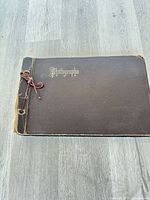 Front cover of brown photograph album showing gilt title and cord binding