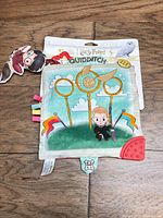 Front of packaged Harry Potter Quidditch soft baby book showing illustration, ribbon tags and teether corner