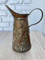 Left side showing embossed seated figure, spout, handle