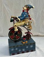 Front view of wooden snowman on bicycle with dog and gifts on decorated base