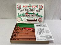 Open box showing logs, roof pieces, gables, instructions, and lid graphic