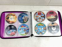Binder open showing first two sleeve pages with eight DVD discs including Spy Kids, Disney Cars and others