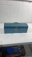 Closed blue metal toolbox on table showing latch and handle