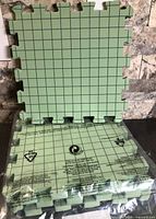 Four green interlocking EVA foam boards, one propped up showing grid side, others stacked in bag