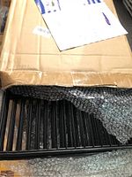Box opened showing stacked black wire grid panels wrapped in bubble wrap