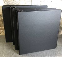 Four black binders standing to show covers and spines