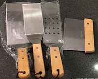 Three stainless steel spatulas with wooden handles plus separate grill scraper