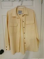 Front of light yellow oversized shirt on hanger showing collar, pockets, buttons