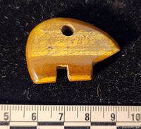 Front view of carved tiger-eye bear pendant on black background with ruler for scale