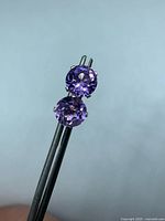 Two round faceted amethyst stud earrings held in tweezers