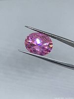 Oval pink cubic zirconia held by tweezers showing brilliant facets