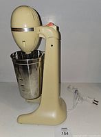 Left side view of cream Hamilton Beach drink mixer with stainless cup and power cord visible