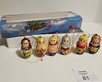 Six nesting doll ornaments displayed in front of open box