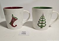 Front view of both Starbucks mugs showing stocking and tree graphics