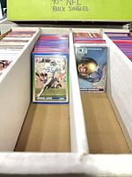 Open four-row card storage box with assorted NFL trading cards including Score Michael Cofer card and London Monarchs helmet card visible