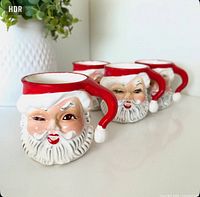 Front view of four winking Santa mugs showing faces and handles