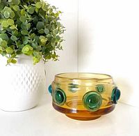 Full view of amber glass bowl next to plant showing exterior applied green prunts