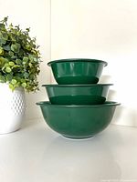 Stacked view of three forest green Pyrex bowls showing size progression and clear bases