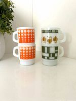 Four stacked Anchor Hocking milk glass mugs, showing orange dot and green patterns