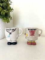 Front view of both themed mugs showing doctor and secretary designs