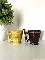 Front view of both McCoy Schering advertising mugs, showing chartreuse and dark brown glazes and Rx emblem