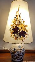 Lamp illuminated, showing ceramic base and pressed-flower shade