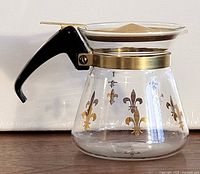 Side view showing carafe, handle, collar, lid, gold fleur-de-lis design