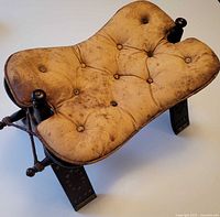 Top angle view of camel saddle stool showing leather cushion wear and overall structure