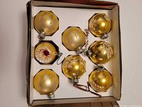 Box with eight gold glass ornaments visible in two rows
