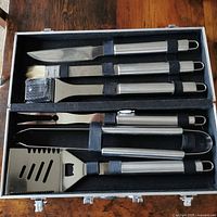 Open aluminum case showing six stainless steel BBQ tools secured by straps
