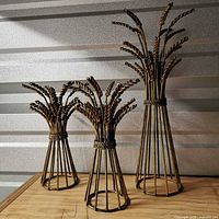Front view of three gold-tone metal wheat sheaf candlestick holders showing size differences