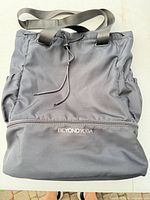 Front view of Beyond Yoga gray drawstring tote showing logo, straps, fabric and overall condition