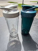 Clear and teal BlenderBottle shaker bottles with lids and wire whisk balls displayed together