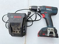 Drill/driver lying beside battery charger showing brand, battery attached and belt clip