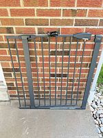 Front view of metal Brica safety gate showing frame, vertical bars, and attached mounting brackets