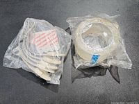 Sealed package containing multiple clear adhesive hooks with adhesive strips alongside sealed roll of clear packing tape
