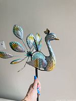 Side view of metal peacock head, body, multicolour tail feathers