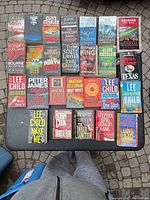 Overhead view of all 26 paperback thriller and crime novels laid out on a table, covers visible