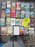 Single image showing all 27 paperback books laid out on paving stones, spines and covers visible for identification.