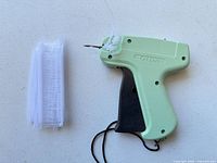 Green OIDA tagging gun with wrist strap and separate bundle of white plastic fasteners on white surface