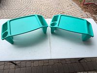 Two turquoise plastic lap trays showing top surfaces, cup holders, side compartments and legs