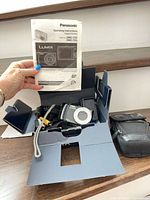 Entire lot in open Panasonic box showing camera, charger, cables, manual, Roots case
