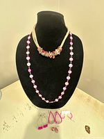 Two necklaces displayed on bust and four pairs of earrings laid out