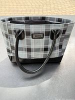 Front view of gray and black plaid Roots insulated lunch bag showing handles and logo plaque