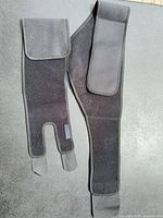 Front view of black Roxofit neoprene lumbar/hip support brace laid flat showing full length strap and closures