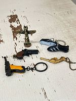 Group shot of all five items: brass totem, Adidas shoe keychain, three weapon keychains