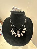Bust displaying two silver-tone necklaces, cameo pendant, triangle bib, and round blue crystal stud earrings
