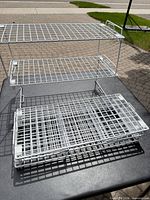 Three white wire shelf risers folded open and stacked